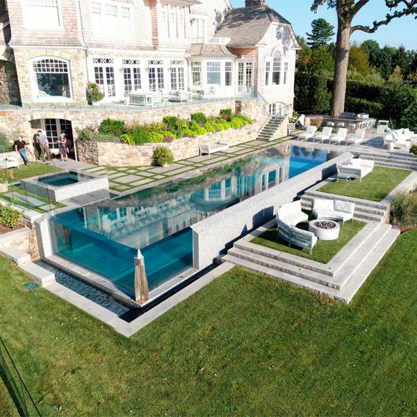 Lujosa piscina infinity con pared transparente, por Drakeley Pool Company, en una casa con un diseño que combina lo moderno y lo clásico