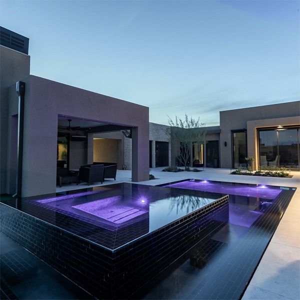 piscina desbordante con spa incorporado en color negro, iluminada por la noche, por Flowing Wells