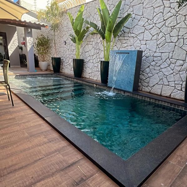 Mini piscina de Igui Fortaleza, revestida de piedra hijau y con una cascada sobre muro en un pequeño patio exterior con suelo en piedra imitación madera