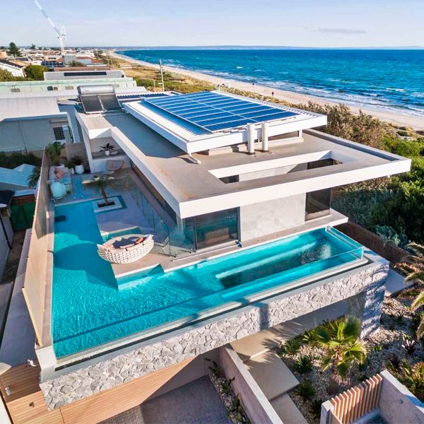 Vista dron de piscina infinita con pared transparente y ventana en el suelo, en un moderno proyecto de casa junto a la playa, por Larsen Homes