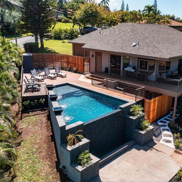 vista dron de piscina infinita de forma trapezoidal, realizada por Maui Pool Masters, y elevada sobre un terreno en pendiente, de una casa unifamiliar