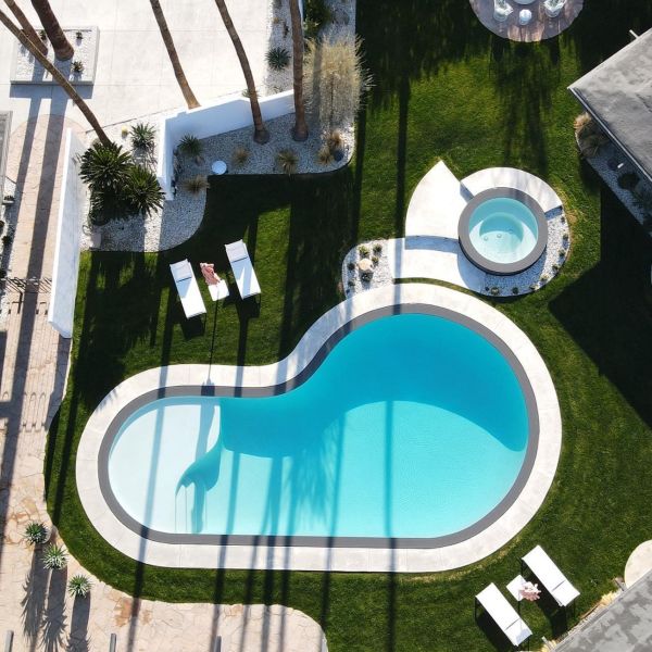 Vista dron de preciosa piscina con diseño en forma de riñón y spa independiente, por MPS Builders, y contrste entre el revestimiento blanco interior y el color oscuro del espacio desbordante