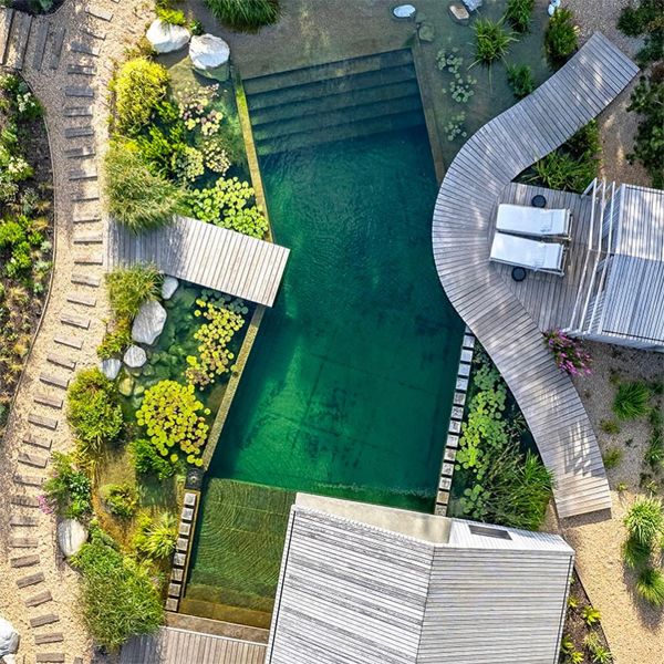 vista dron de una piscina natural, de diseño geométrico, en el que la madera y las diferentes plantas toman el protagonismo, por Natural Swimming Pools Ltd