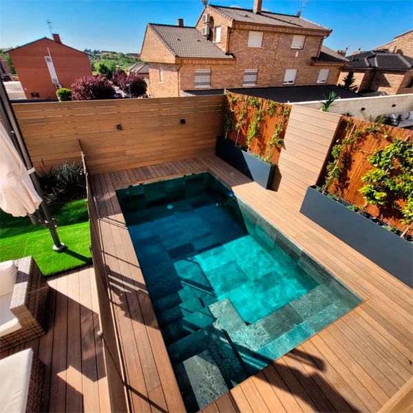 piscina privada de diseño clásico y revestimiento en gres porcelánico, rodeada de tarima de madera sintética, en un proyecto de Piscinas Los Hermanos