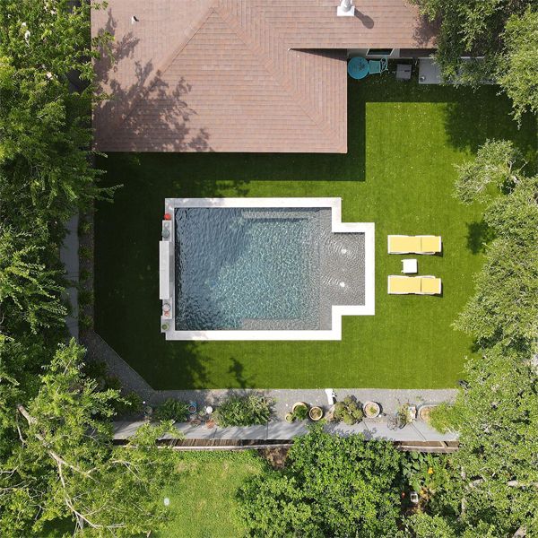 Vista dron de mini piscina de diseño clásico, basado en líneas rectas y revestimiento en color gris oscuro, por Texas Tiny Pools, en un jardín privado con césped artificial
