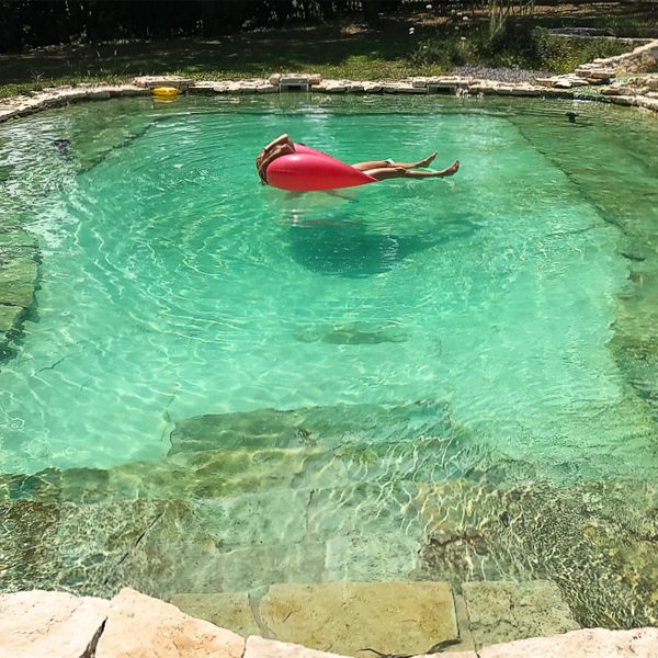 mujer flotando en el agua de una piscina natural con piedra interior