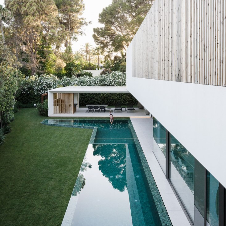 hombre lanzándose a una moderna piscina en forma de L, revestida de piedra bali en un moderno proyecto de casa por 969 Arquitectos