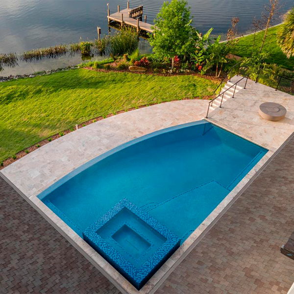 Vista dron de piscina infinity a medida, con spa integrado, por All Custom Pools, situada junto al lago