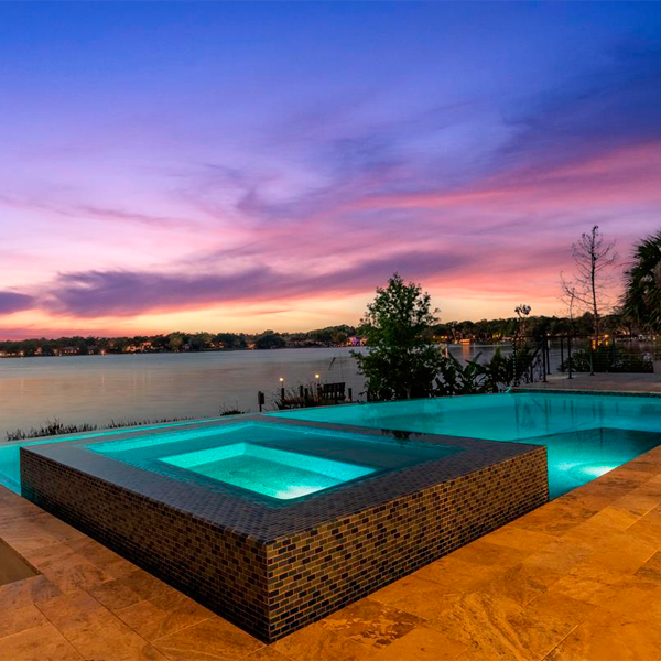 piscina infinity a medida, con spa integrado, por All Custom Pools, iluminada al atardecer, con espectaculares vistas al lago