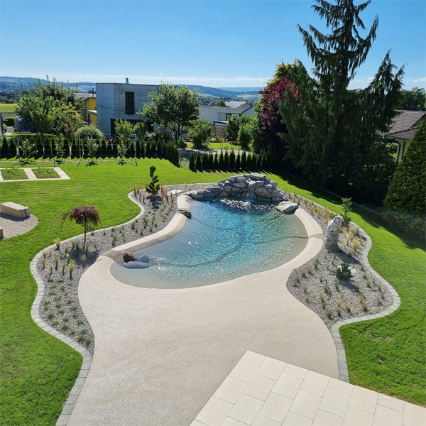 Vista dron de piscina playa a medida, con una cascada sobre las rocas, en un jardín personalizado de gran tamaño, por Biodesign Pools Deutschland