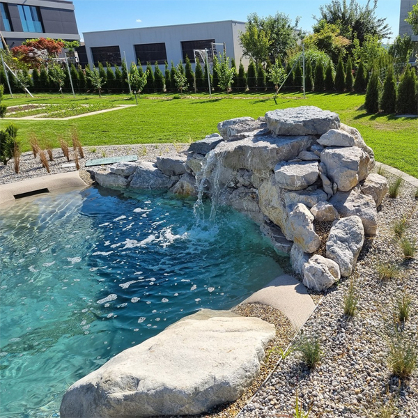 Cascada sobre las rocas de una piscina estilo playa, de Biodesign Pools Deutschland