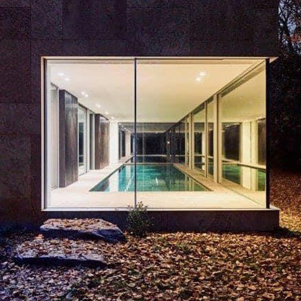 Piscina interior de diseño minimalista, vista por la noche desde el exterior, a través de los grandes ventanales de este proyecto de DDM Architectuur