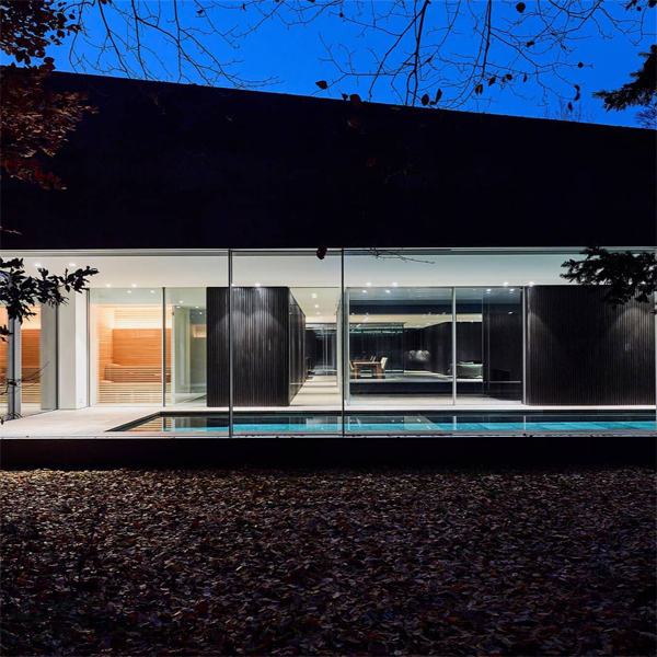 Piscina interior de diseño minimalista, vista desde el exterior, a través de los grandes ventanales de este proyecto de DDM Architectuur