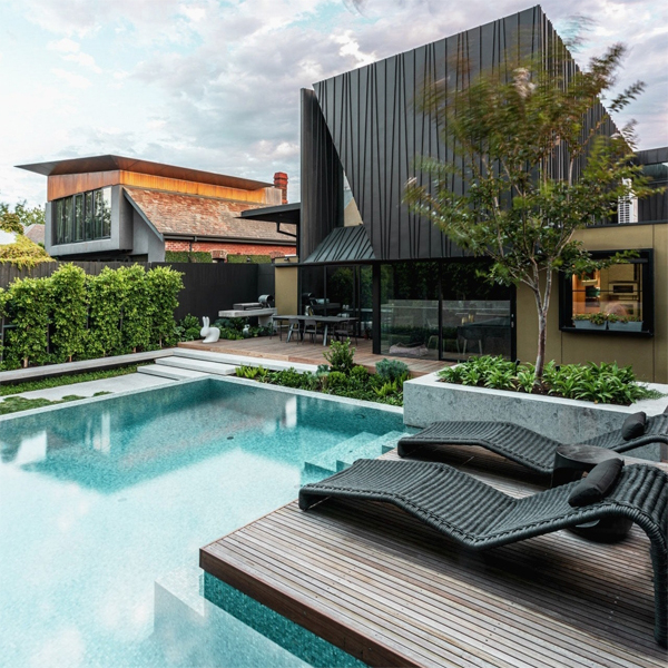 piscina infinita de diseño depurado a medida, por Feature Pools, en una casa de diseño moderno, con pequeña terraza de madera y una gran combinación de materiales en el jardín