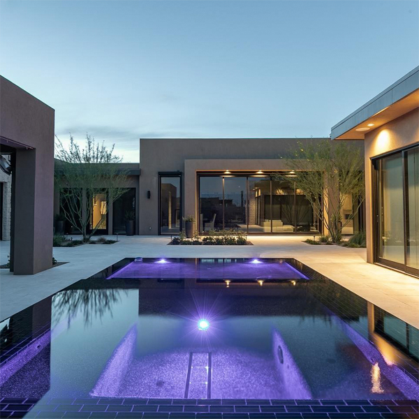 piscina desbordante con spa incorporado en color negro, iluminada por la noche, por Flowing Wells