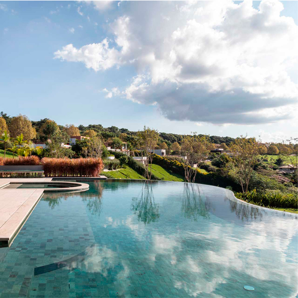 Piscina infinita donde se reflejan la nubes del cielo, en un proyecto de Gilda Meirelles Arquitetura, en medio de una colina