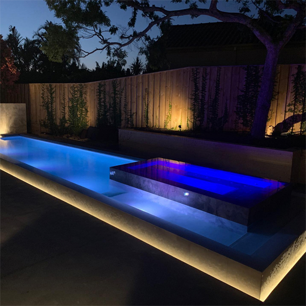 piscina minimalista con un spa incorporado en color contraste, por Graziani Pools, en un jardín de diseño moderno, iluminado por la noche