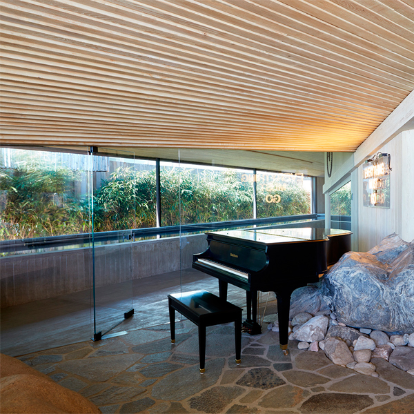 piscina interior de diseño minimalista, estilo canal de natación, en un proyecto de Kovac Design Studio, vista desde un salón interior con un piano