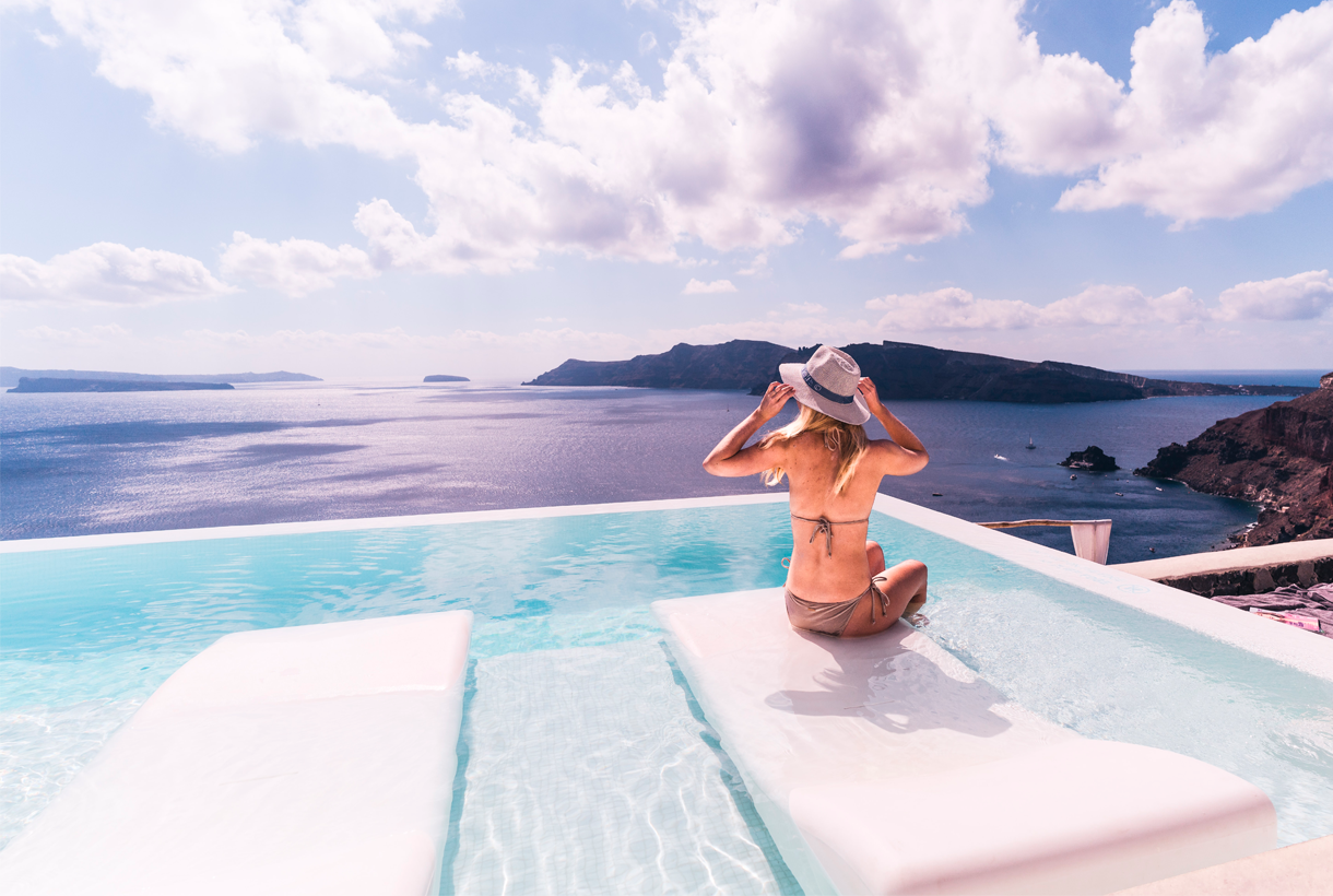 mujer sentada en una tumbona dentro de una piscina infinity mirando el horizonte