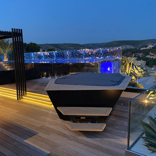 exclusiva piscina infinity con pared transparente, instalada en un rooftop, por la noche, de Le Bassin Francais