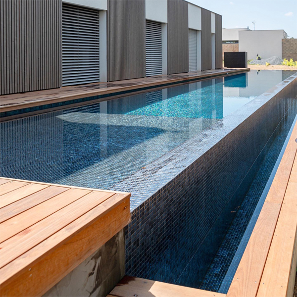 Piscina infinita, estilo canal de natación, por MCR Piscines, y terraza en tarima de madera, en un espacio de diseño industrial