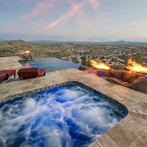piscina infinity a medida y spa, por Morris Pools, rodeados de piedra natural y juegos de fuego, con espectaculares vistas al atardecer