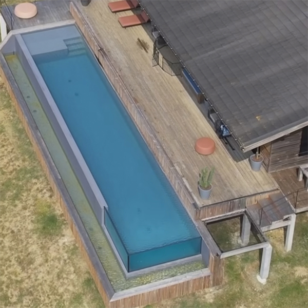 Vista dron de piscina infinta con paredes transparentes y diseño ideal para nadar, en una casa con terraza de madera, dentro de un proyecto de Aloha Concepteur Exterieurs