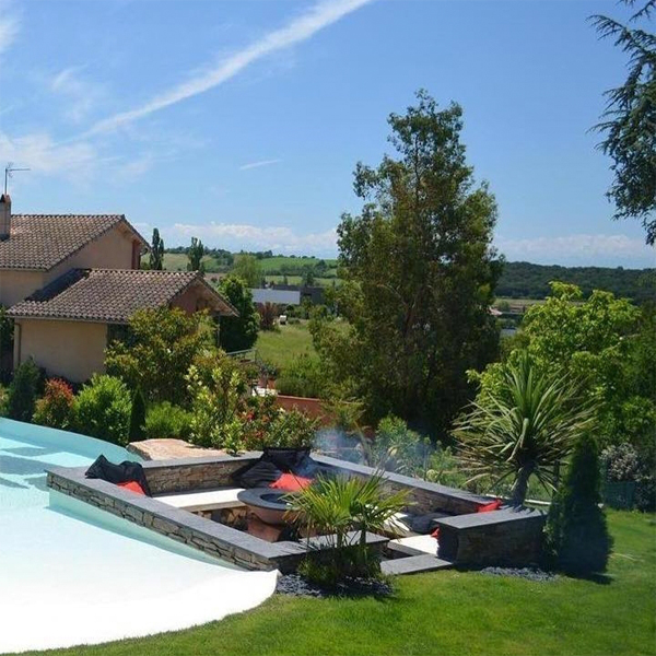 Salón exterior junto a una piscina estilo playa con desbordante infinito, en un jardín privado, por Piscines Iloé