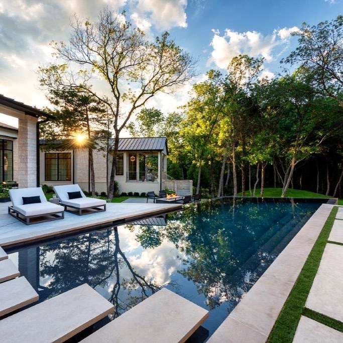 Piscina infinita de diseño en líneas rectas y ángulos, con revestimiento en color oscuro, por Pool Environments, con pasos flotantes en la superficie y una zona solarium con tumbonas