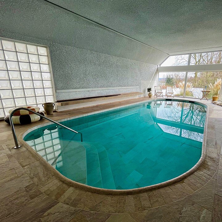 Piscina interior a medida, por Sankurt Germany, rodeada de gres porcelánico, con un diseño minimalista de estilo rústico