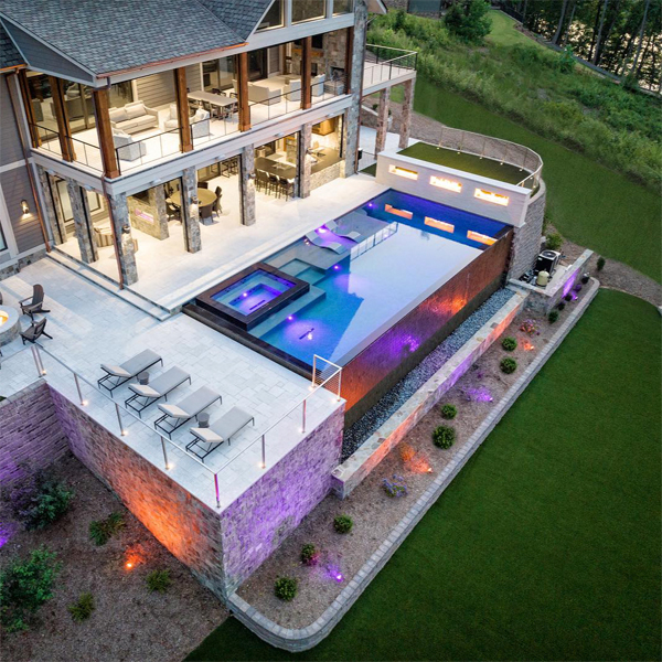 Espectacular vista aérea de una piscina infinita de lujo, con spa integrado, de Signature Luxury Pools, iluminada con focos led, al atardecer