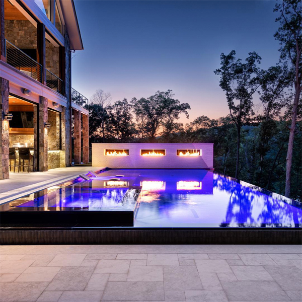 piscina infinita, efecto espejo, con spa integrado, de Signature Luxury Pools, iluminada por la noche y con pequeñas hogueras en muro exterior