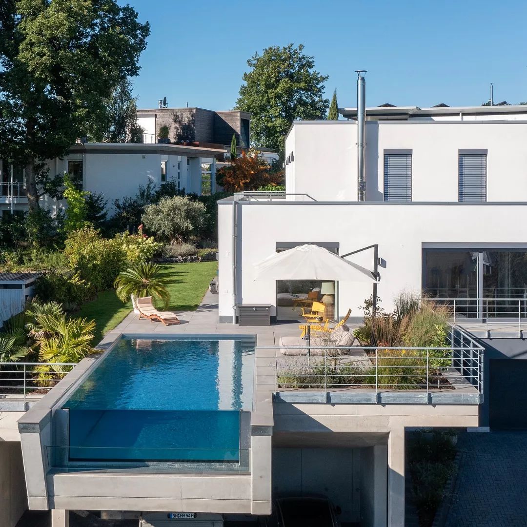 Vista dron de una piscina volada, de diseño minimalista, con un extremo transparente desbordante, estilo infinity, por SSF Pools by KLAFS