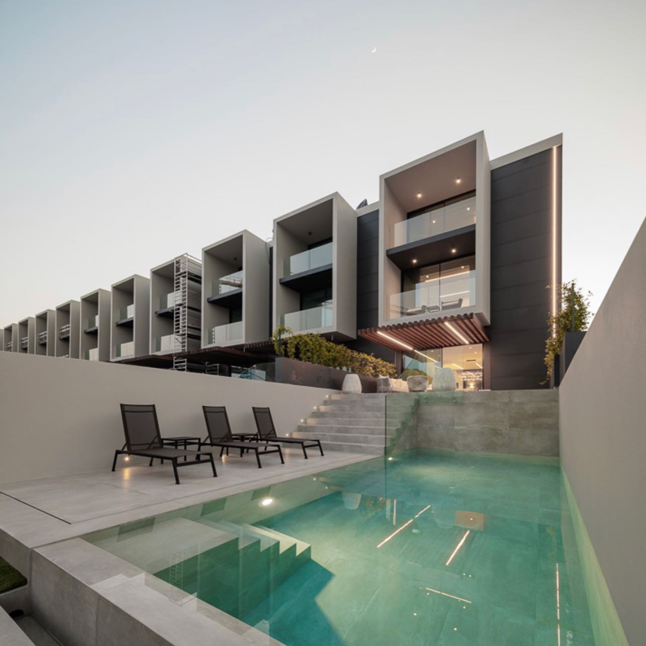 Piscina infinita moderna y minimalista, iluminada al atardecer, en proyecto de Unique Build