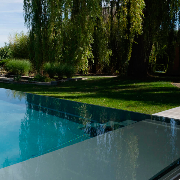 piscina infinita en acero inoxidable, por Van Eeckhoudt Pools, en un jardín con gran número de árboles