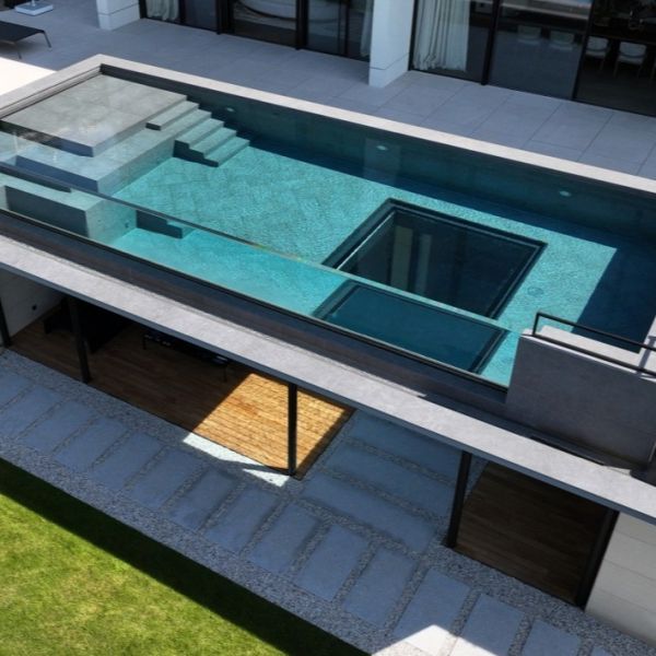 Vista aérea de una lujosa piscina transparente, de diseño rectangular, con una ventana subacuática de forma cuadrada, por Holland Aqua Sight, en el suelo.
