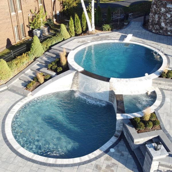 Vista dron de piscina a dos niveles realizada por Coastal Pools, en el que una piscina de diseño circular desborda sobre otra también circular, y mini spa