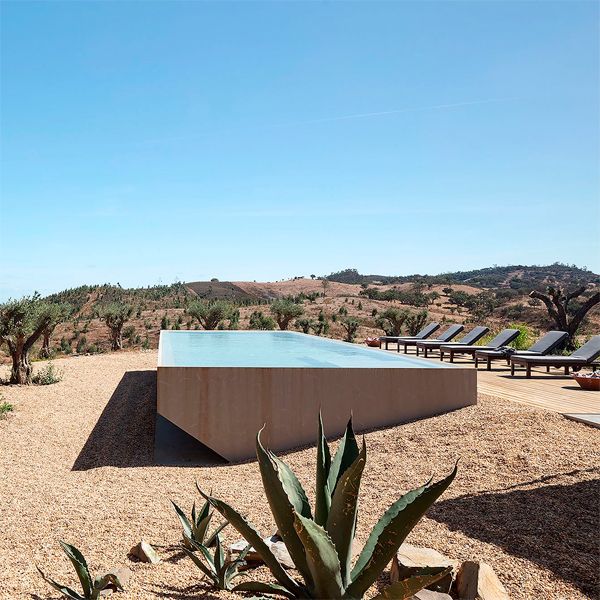 Une piscine à débordement au design unique, de style monobloc, avec un côté légèrement surélevé dans un projet en pleine campagne, par Promontorio
