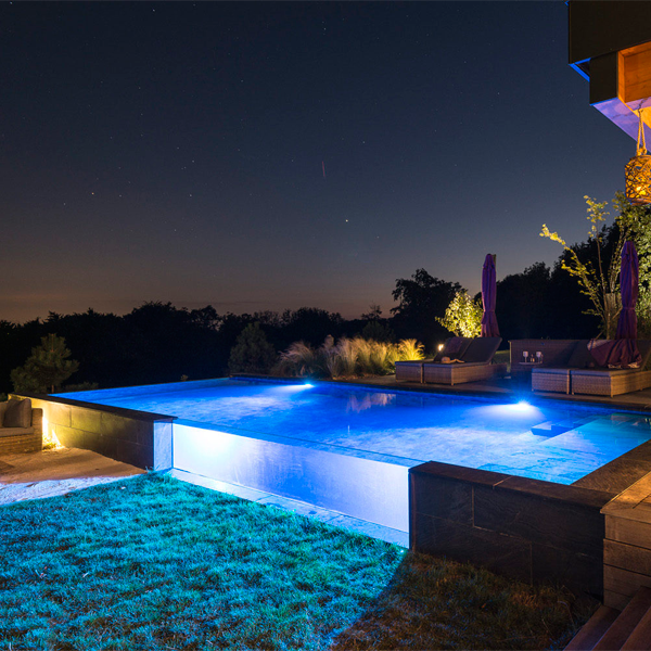 piscine hors sol à débordement avec parois vitrée la nuit par Atelier Olea