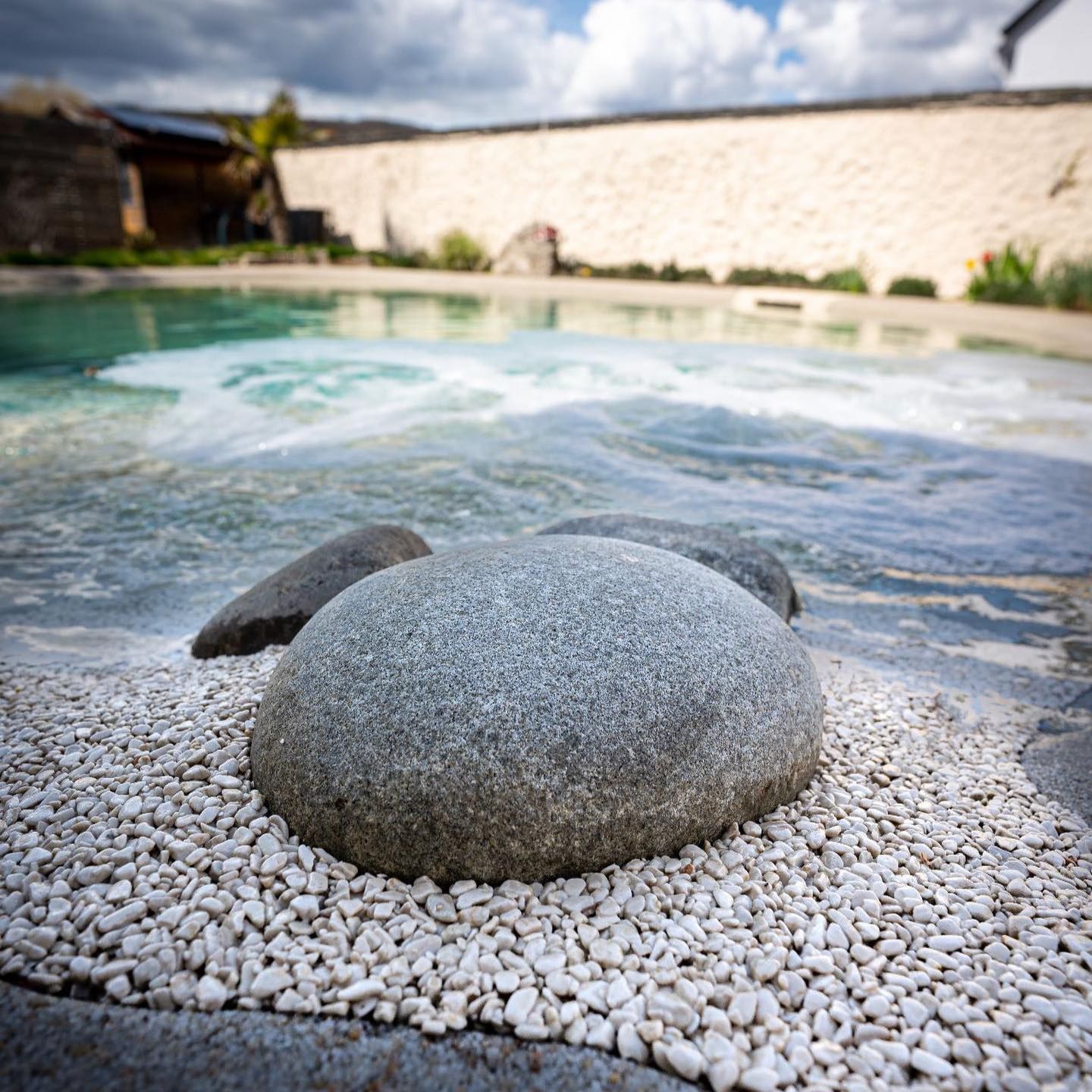 Détail de pierre et de sable dans une piscine naturelle Biodesign, style plage, réalisée sur mesure dans un petit jardin privé, par Gartengestaltung Sven Pfadt