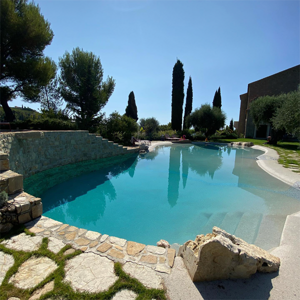 piscine style plage sur mesure, par Piscine Sorgiva, entourée de pierre, d'arbres et de végétation, dans une maison de campagne