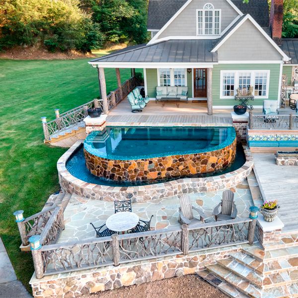 Vue drone d´une mini piscine spa à débordement sur mesure, avec un certain air rustique grâce à son revêtement extérieur en pierre, par Crystal Pools