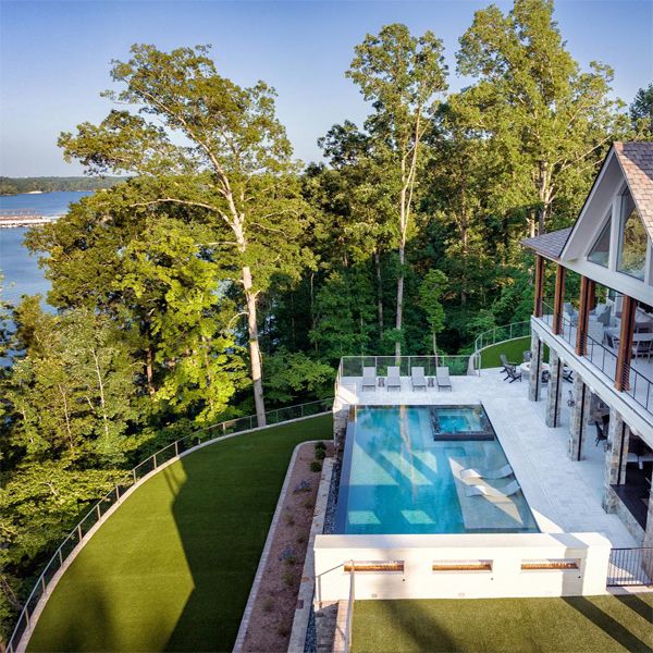 Vue drone d´une spectaculaire piscine à débordement par Signature Luxury Pools, dans une maison moderne avec beaucoup de végétation et de superbes vues sur le lac