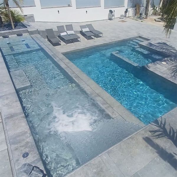 une piscine unique, avec des espaces spa, divisée en deux niveaux, par Pool Jump, dans un espace monochrome en grès cérame, tant à l'intérieur qu'à l'extérieur