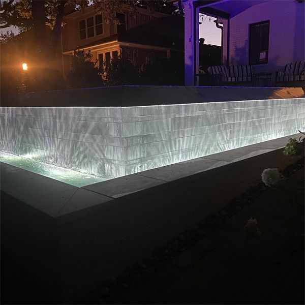 revêtement d´une en gris, d'une belle piscine à débordement, par Pure Design, illuminée la nuit, vue de l'extérieur