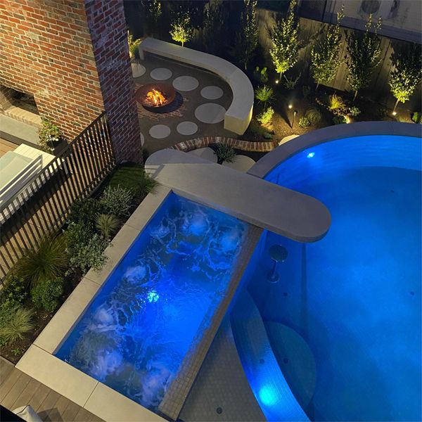 vue drone d´une piscine unique avec spa intégré, par Exquisite Pools and Gardens, éclairée la nuit