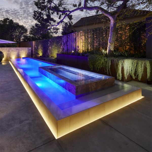 piscine minimaliste à débordement éclairée et spa, par Graziani Pools dans un jardin moderne la nuit