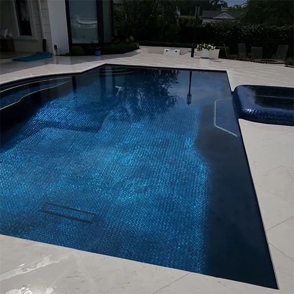 Piscine sur mesure avec spa à débordement, dans laquelle se distingue son revêtement en carreaux de verre bleu vif, par Hampe Pools