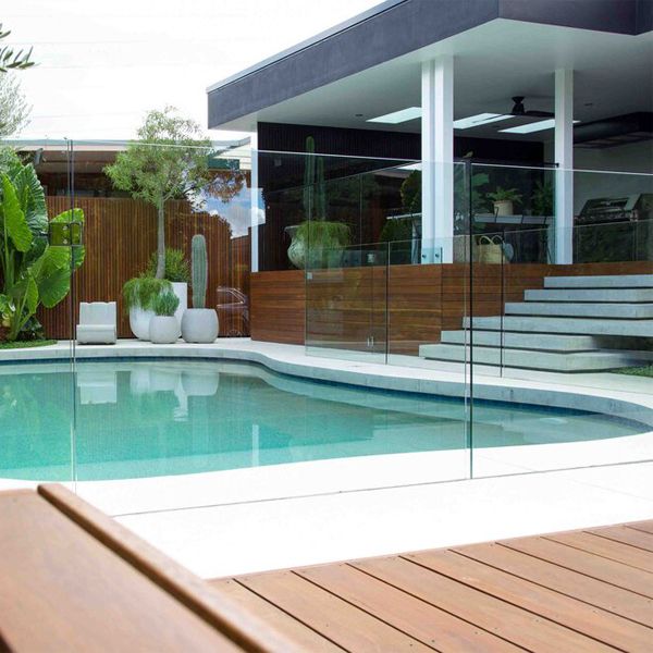 piscine privée sur mesure, au design courbé, par Impressions Pools, avec une clôture en verre transparent qui la sépare de la terrasse en bois