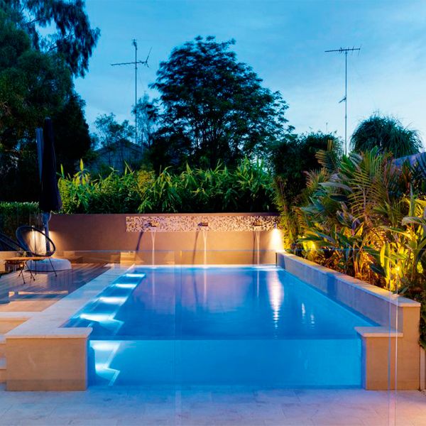 piscine privée semi-enterrée avec paroi transparente, par Jade Pools, éclairée la nuit